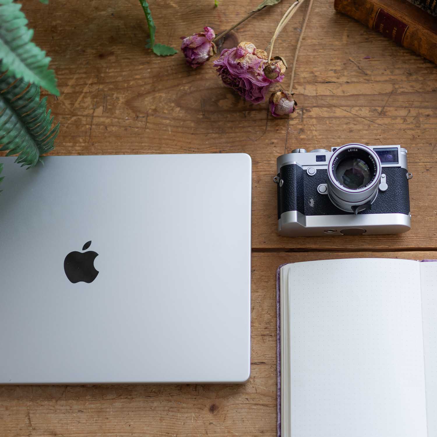 MacBook, Notizbuch und Kamera auf Holztisch
